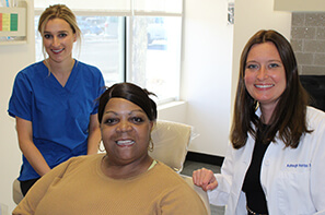 female dental assistant in blue shirt, female dental patient wearing tan shirt and female dentist wearing white lab coat