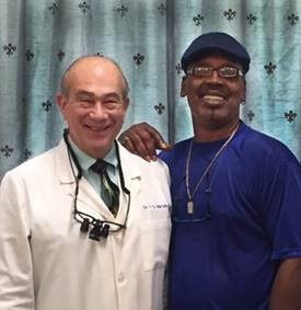 older white male dentist in lab coat on the left and older gentleman DDS patient African American in blue shirt on the right