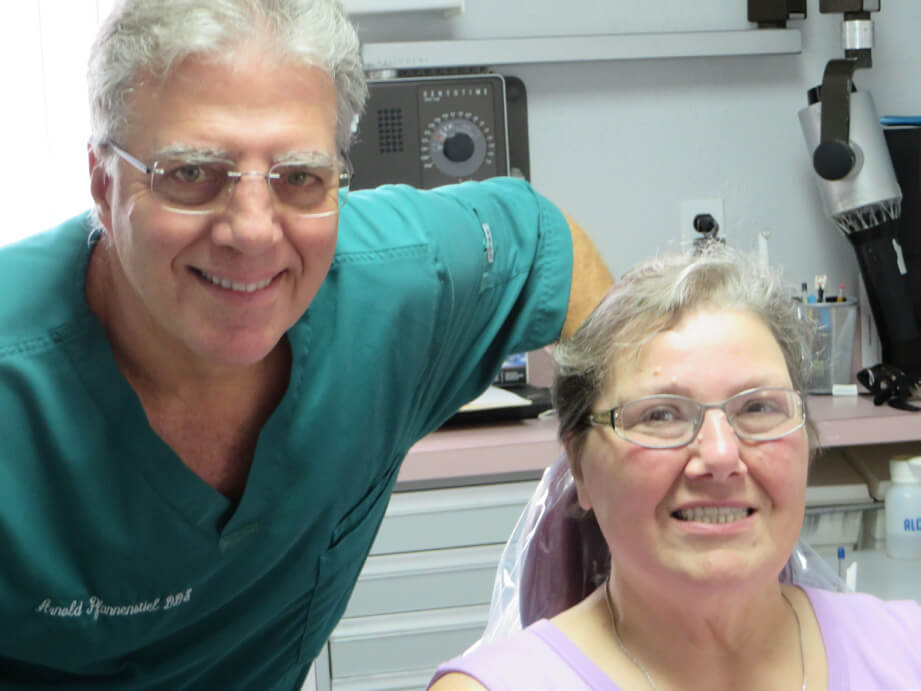 Older male dentist in green scrub and older woman patient in pink shirt